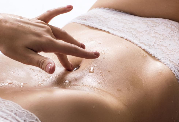 Faire squirter une femme - Main féminine caressant le ventre d'une femme portant des sous-vêtements, avec des gouttes de liquide sur la peau.