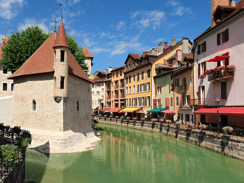 Massage érotique Annecy - Vieille ville d'Annecy avec le Palais de l'Île et les maisons colorées le long du canal, sous un ciel bleu clair.