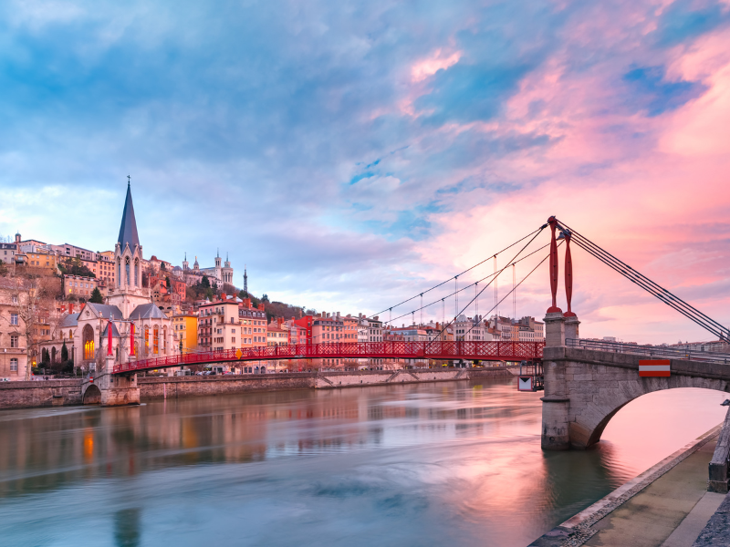 Massage érotique Lyon - Vue du pont rouge Saint-Georges et de l'église Saint-Georges à Lyon, au coucher du soleil, avec la Saône reflétant les couleurs du ciel.