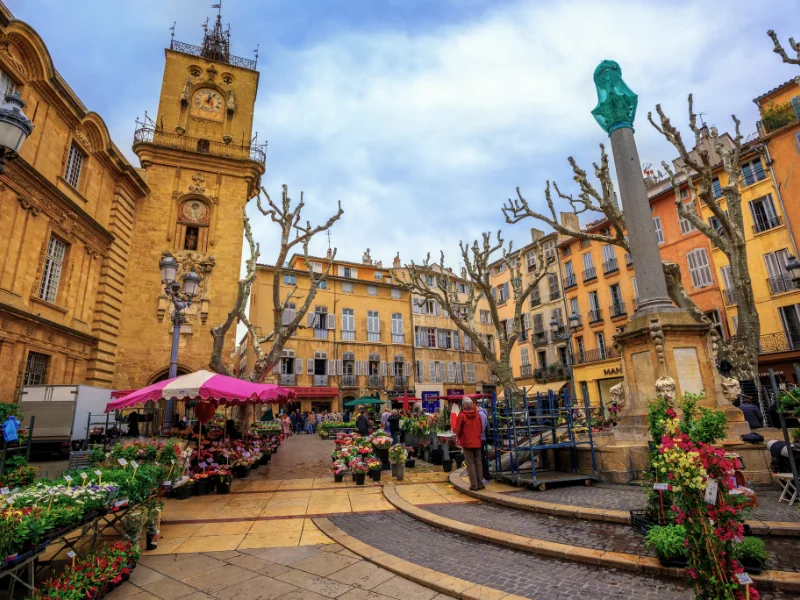 Massage érotique Aix-en-Provence - Place colorée avec un marché aux fleurs à Aix-en-Provence, devant l'Hôtel de Ville avec son horloge ancienne.