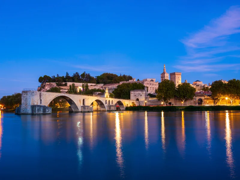 Massage érotique Avignon - Vue nocturne du Pont Saint-Bénézet et du Palais des Papes à Avignon, avec leurs reflets illuminés dans le Rhône.