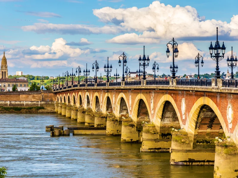 Massage érotique Bordeaux - Vue du Pont de Pierre à Bordeaux, un pont en briques rouges avec des arches majestueuses, traversant la Garonne sous un ciel partiellement nuageux.