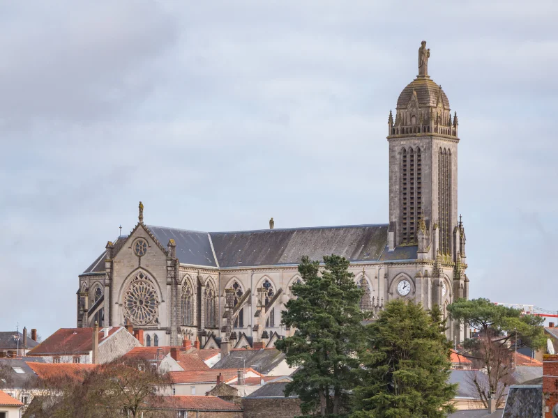 Massage érotique Cholet - Vue de l'église Notre-Dame de Cholet, avec son architecture néogothique et son imposante tour clocher au-dessus des toits des maisons environnantes.