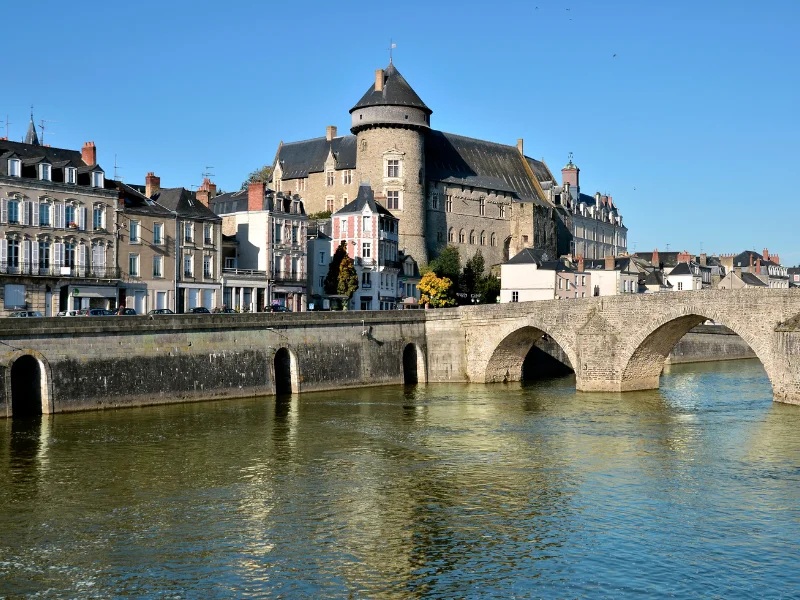 Massage érotique Laval - Vue sur le château de Laval et le pont Vieux au bord de la Mayenne sous un ciel bleu dégagé.