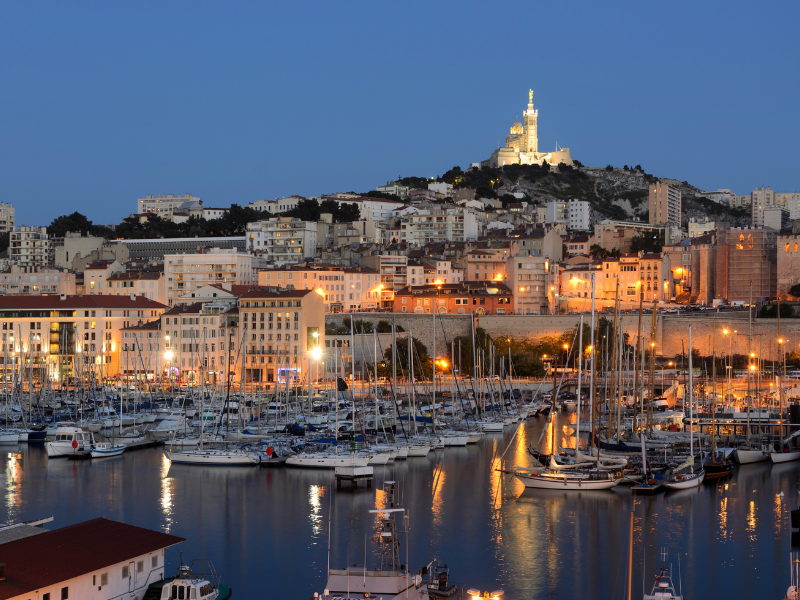 Massage érotique Marseille - Vue nocturne du Vieux-Port de Marseille avec ses bateaux amarrés, et la basilique Notre-Dame de la Garde illuminée en arrière-plan.