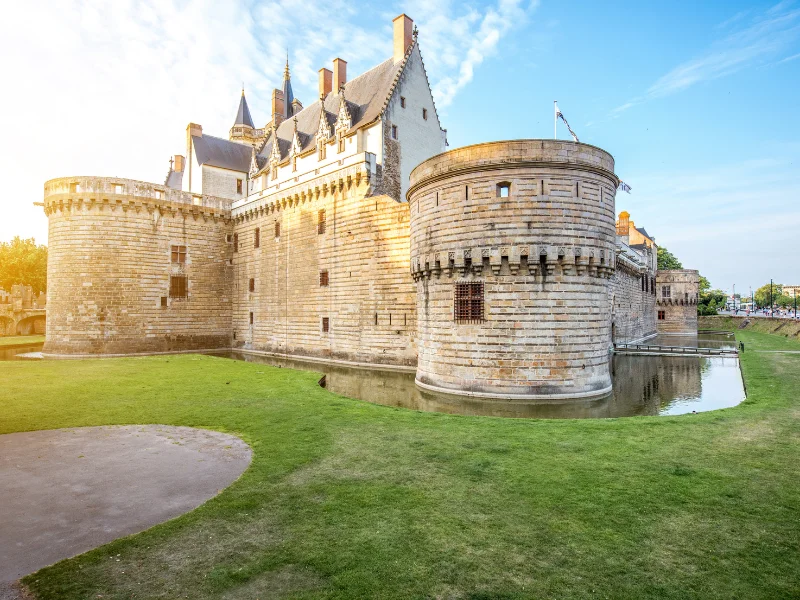 Massage érotique Nantes - Vue extérieure du Château des Ducs de Bretagne à Nantes, France, au coucher du soleil avec douves et tours rondes en pierre.