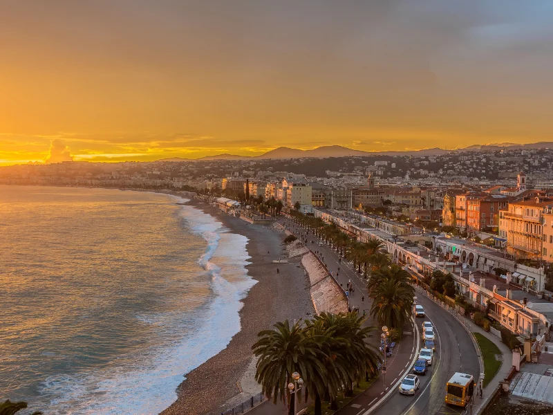 Massage érotique Nice - Vue sur la Promenade des Anglais à Nice au coucher du soleil avec la mer Méditerranée et des bâtiments longeant le bord de mer.