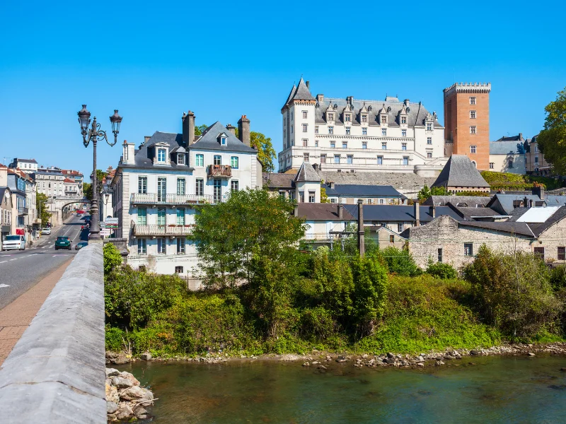 Massage érotique Pau - Vue du château de Pau surplombant des maisons traditionnelles et une rivière sous un ciel bleu clair.