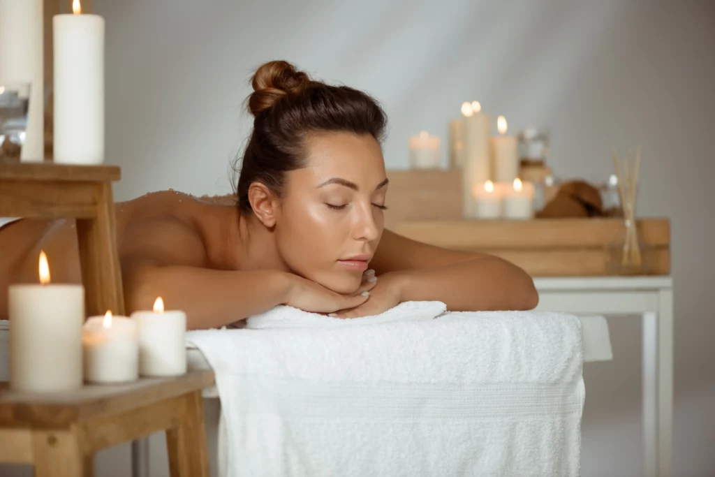 Femme allongée sur une table de massage, entourée de bougies allumées, créant une ambiance relaxante et apaisante.