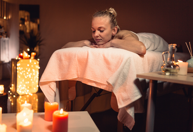 Massage tantrique pour femme - Femme se détendant sur une table de massage entourée de bougies allumées, dans une ambiance tamisée.