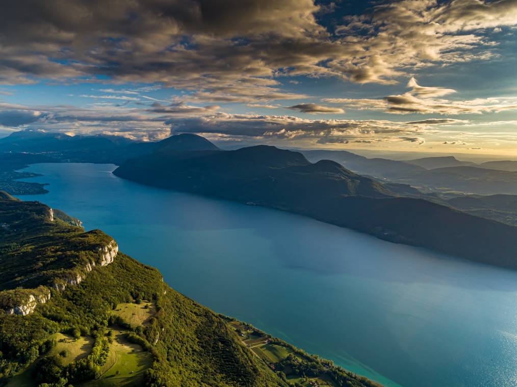 massage érotique aix-les-bains : Vue aérienne du lac du Bourget à Aix-les-Bains au coucher du soleil, entouré de montagnes et de verdure.