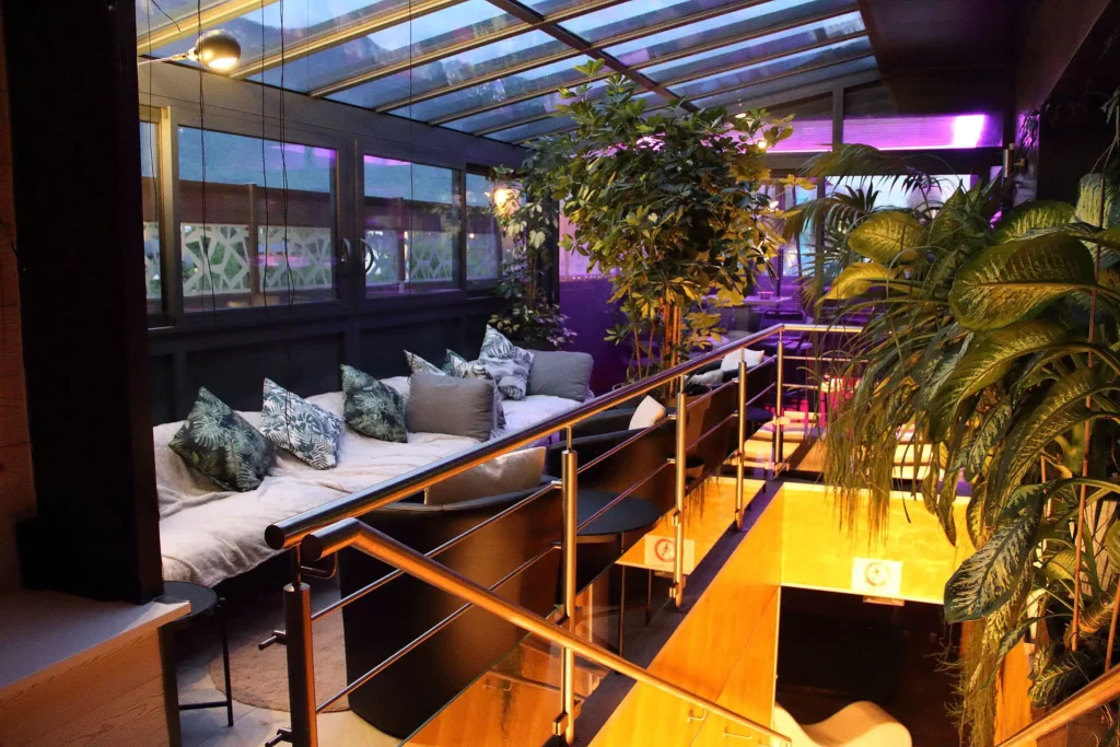 Espace détente intérieur des Jardins de Bao avec canapés, coussins et plantes sous verrière
