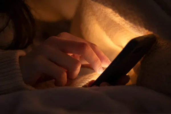Main de femme qui écrit sur son téléphone, sous la couverture